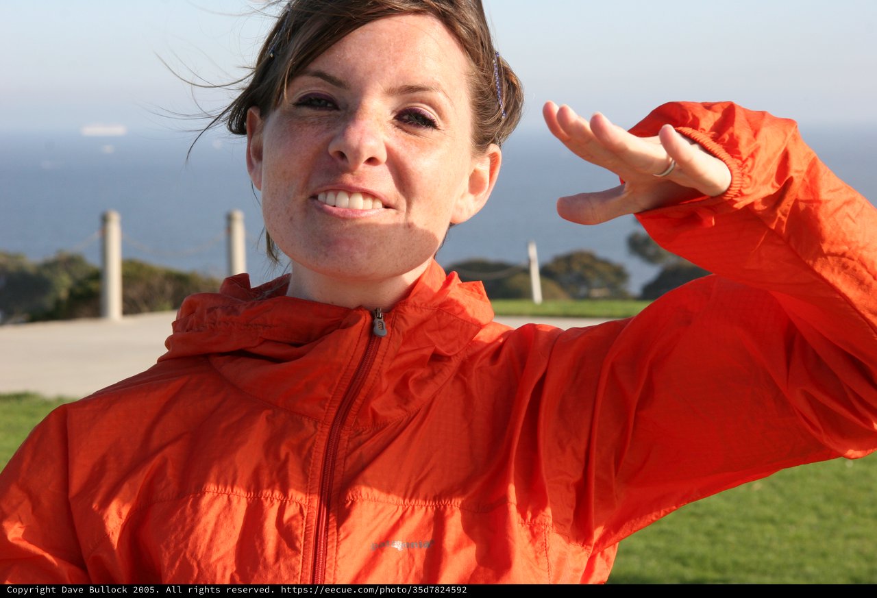 Woman in Orange Jacket Poses by the Coast