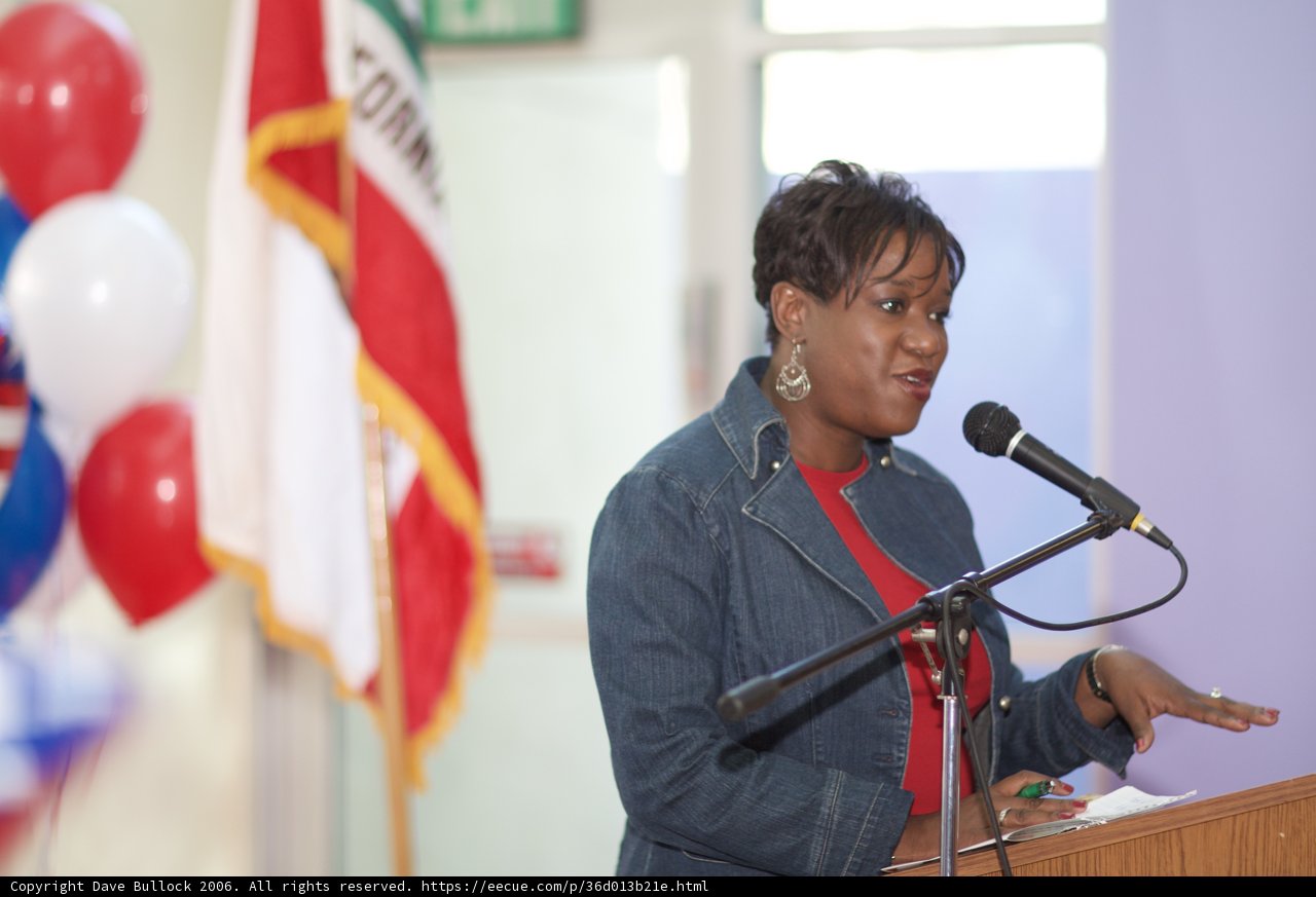 Woman Addressing Crowd with Flag in Background
