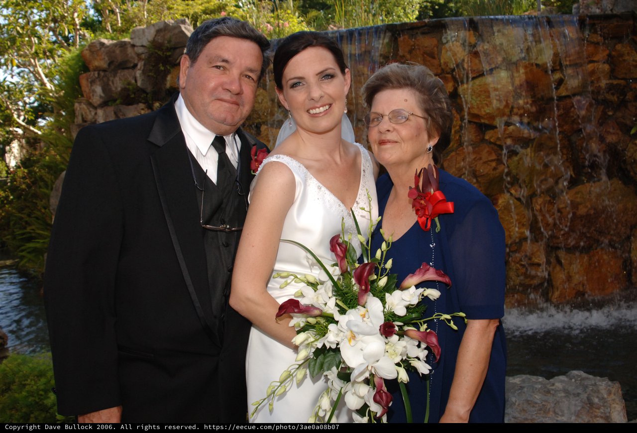 Bride Poses with Parents at Waterfall Wedding Venue