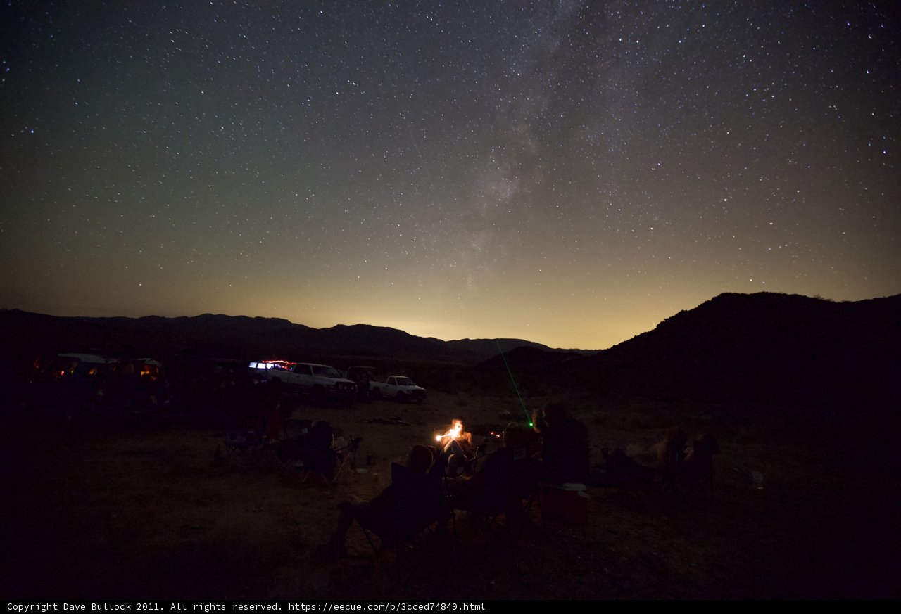 Under the Starry Night Sky Caption: Campers gather around a cozy campfire, under a dazzling night sky filled with stars and the Milky Way.