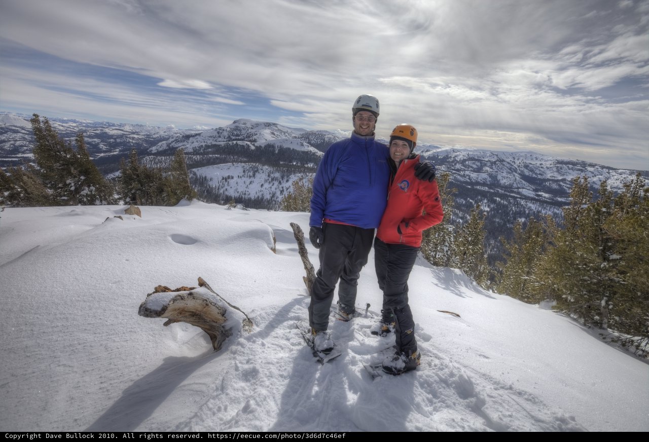 Summit Smiles: Couple Atop Snow-Covered Mountain Peak