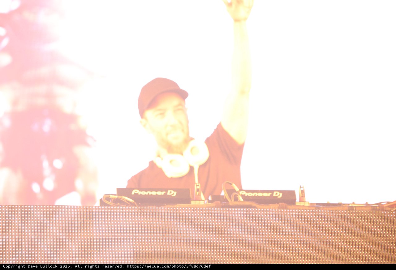DJ Raises Hand Amid Blazing Stage Lights at Festival