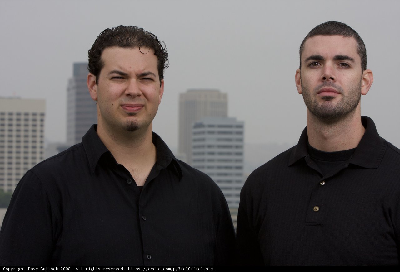 Two Happy Men in Black Shirts Pose in Front of Skyscraper