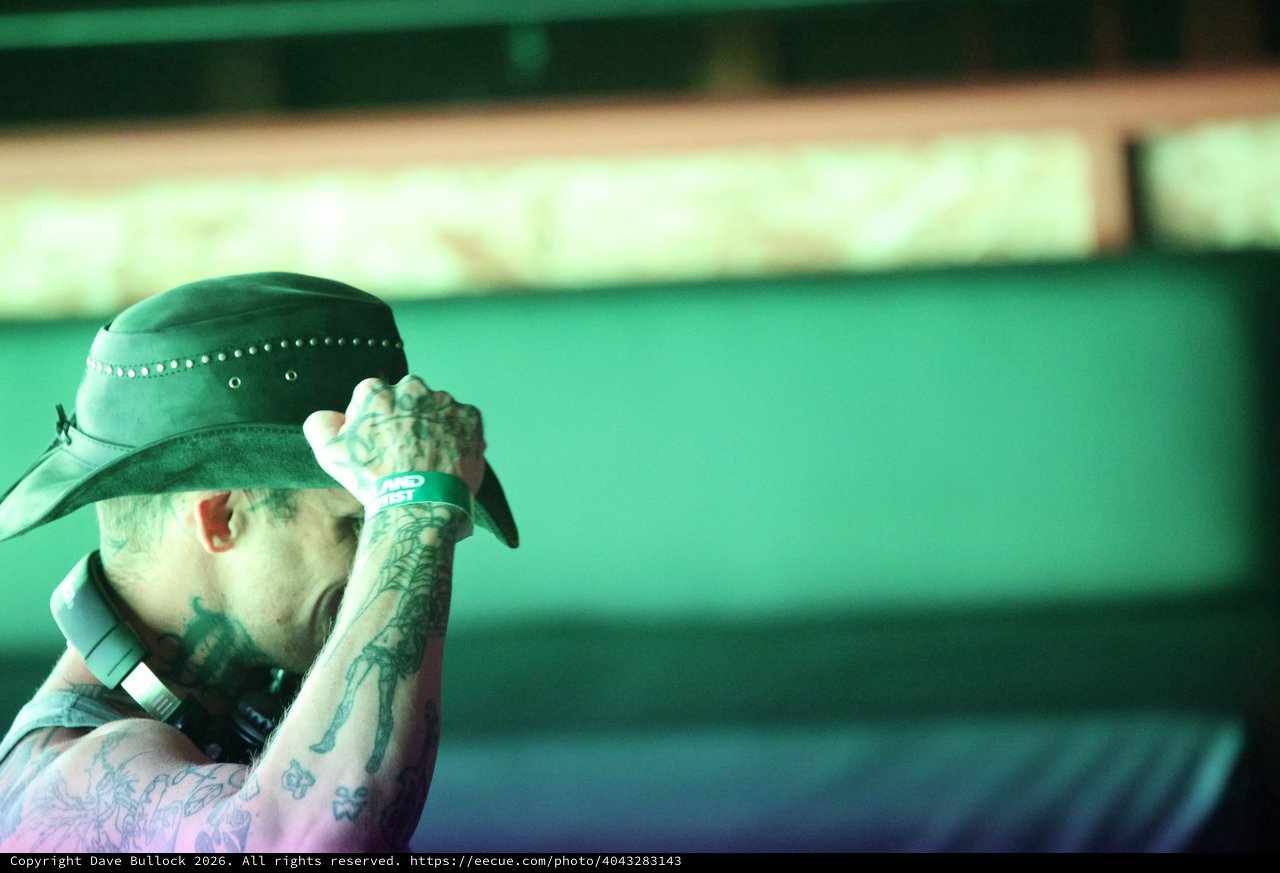 Tattooed Performer Tips Hat Under Green Stage Lights