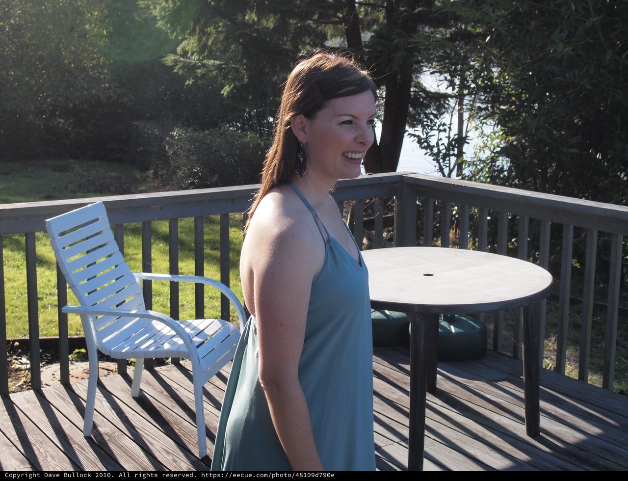 Woman in Teal Dress Smiling on Sunny Deck