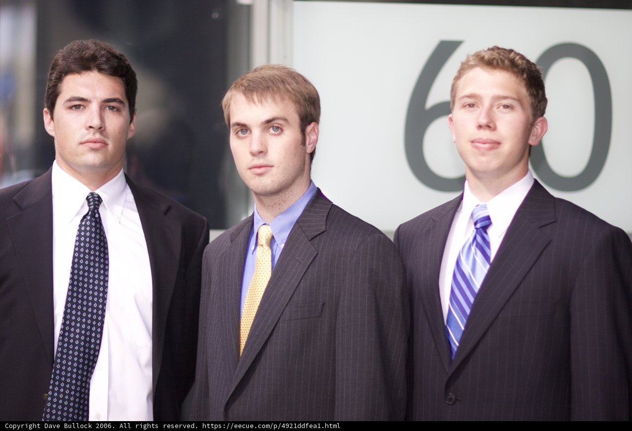 Three Men in Suits Pose in Front of a Sign