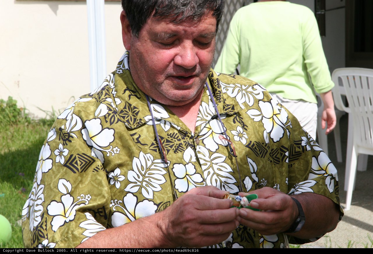 Man in Hawaiian Shirt Examining Small Object Outdoors