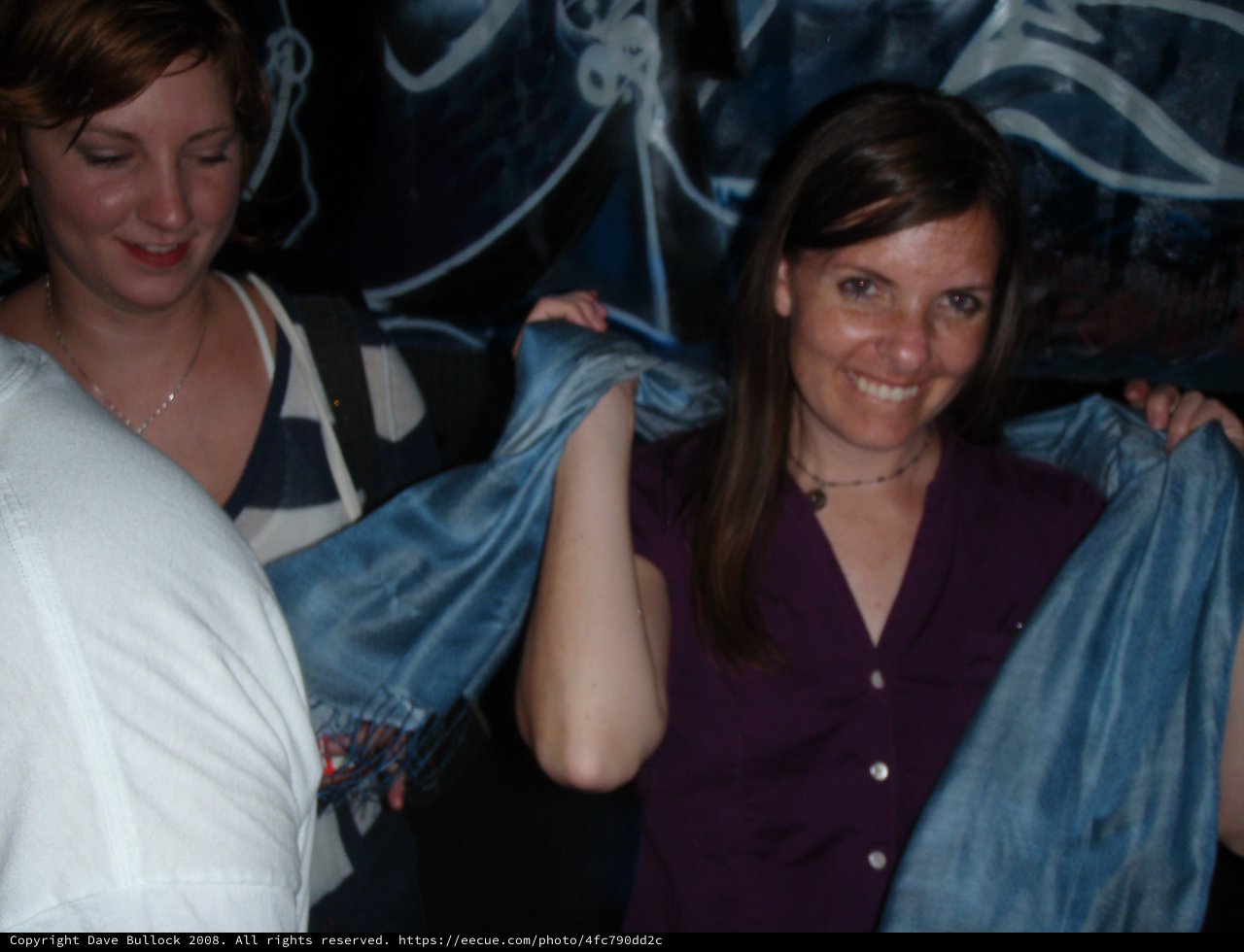 Two Women Holding Blue Fabric at Nighttime Event