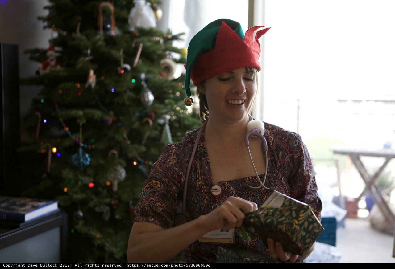 Holiday Elf Nurse Opening Christmas Gift with Joy