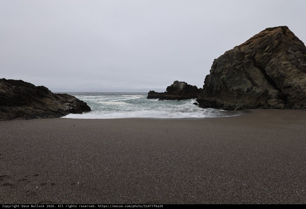 Secluded Cove with Dark Sand and Crashing Waves