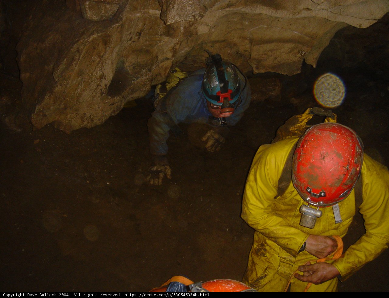 Exploring the Depths Caption: Two workers don their hardhats to venture into the depths of a cave, surrounded by the rugged beauty of nature's rocks.