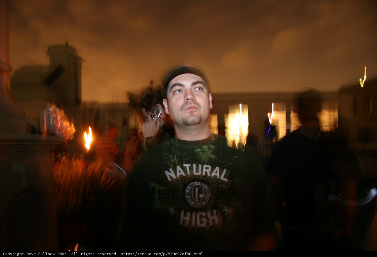 Green Shirted Man Gazes into Fiery Vigil