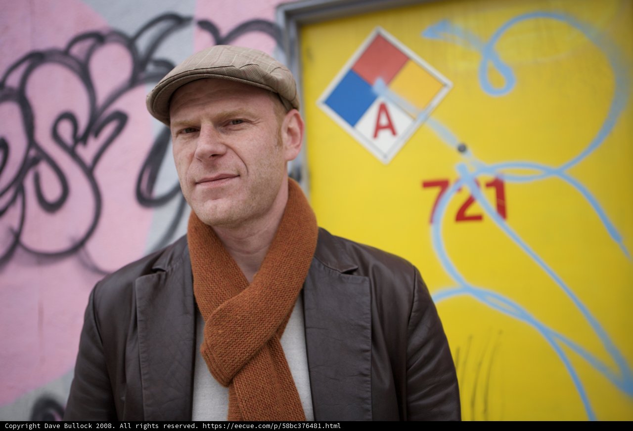 Man in Hat and Scarf in Front of Colorful Building