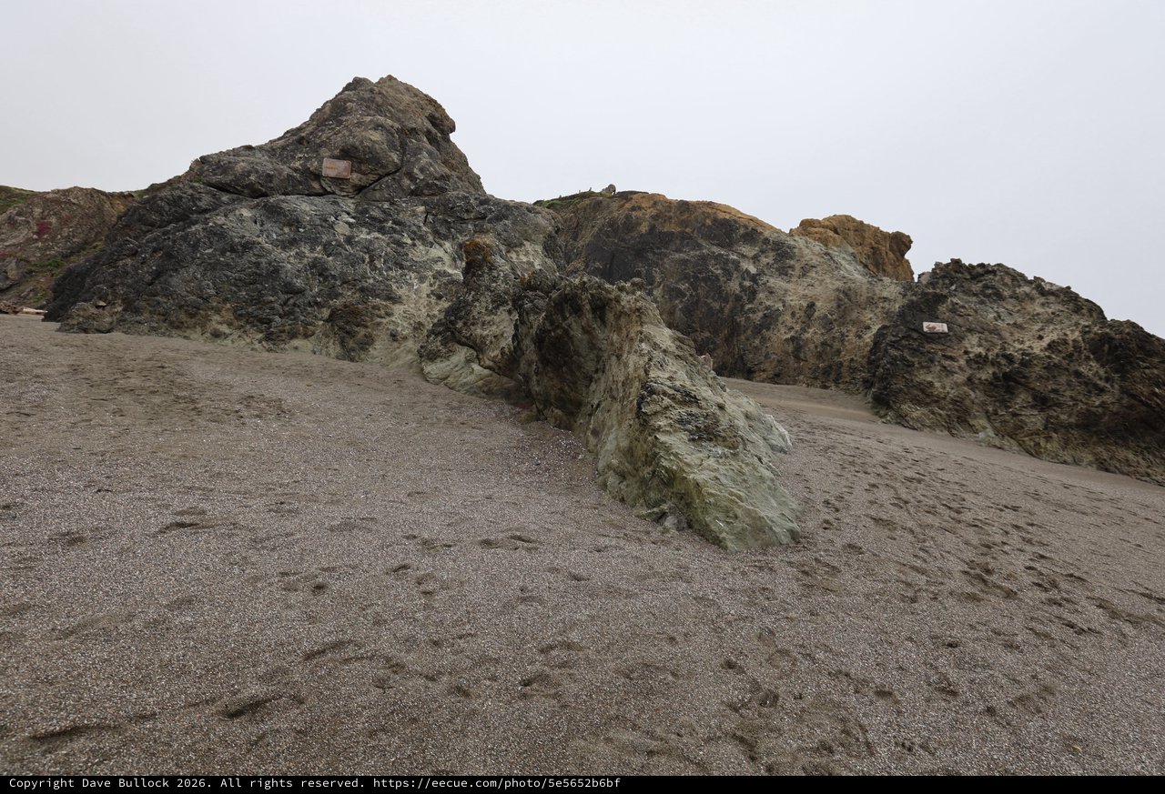 Ancient Coastal Rocks Emerging from Gray Sandy Beach