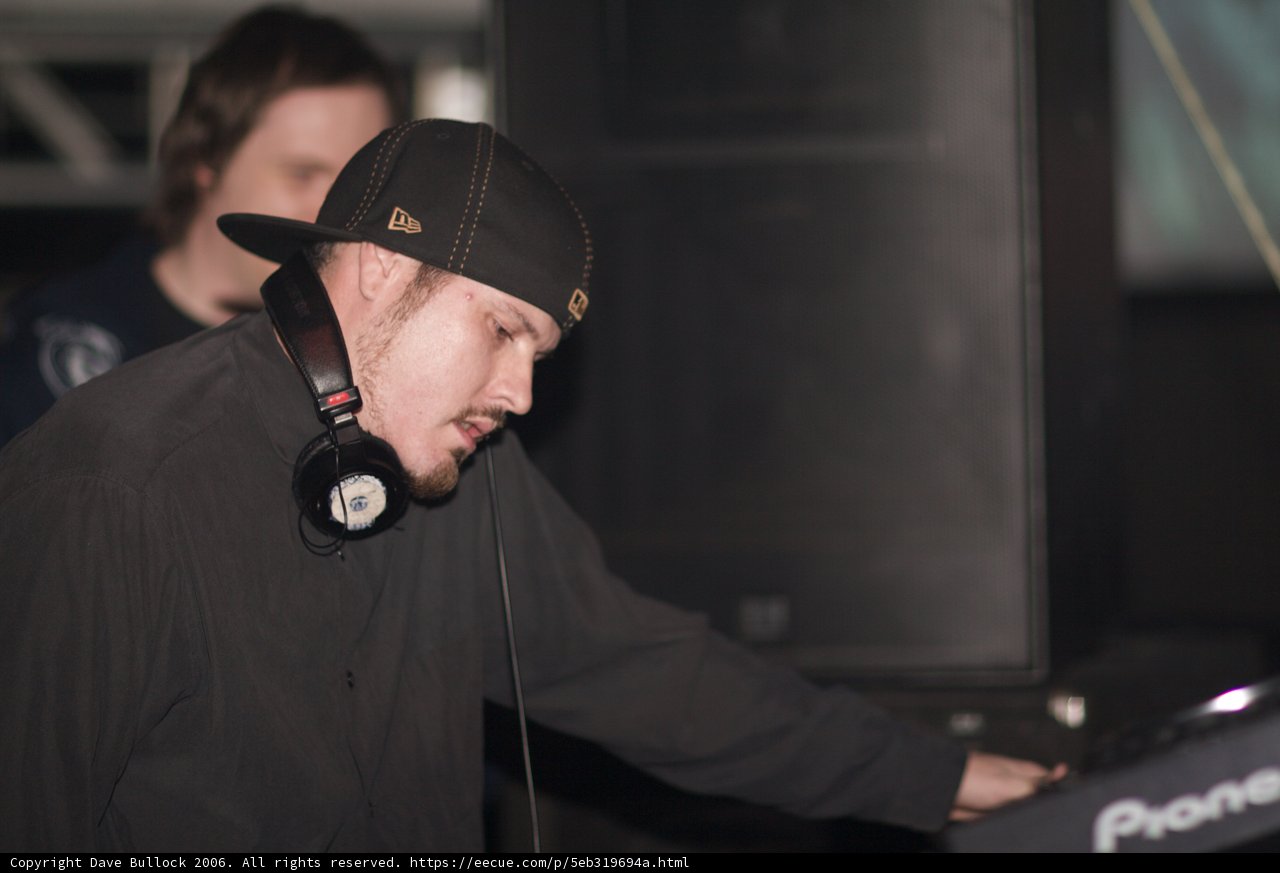 Black Shirted Travis B Wears Baseball Cap and Headphones