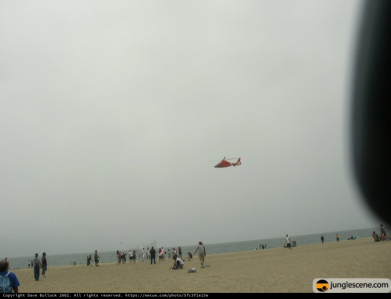 Red Helicopter Soaring over Beach-Goers