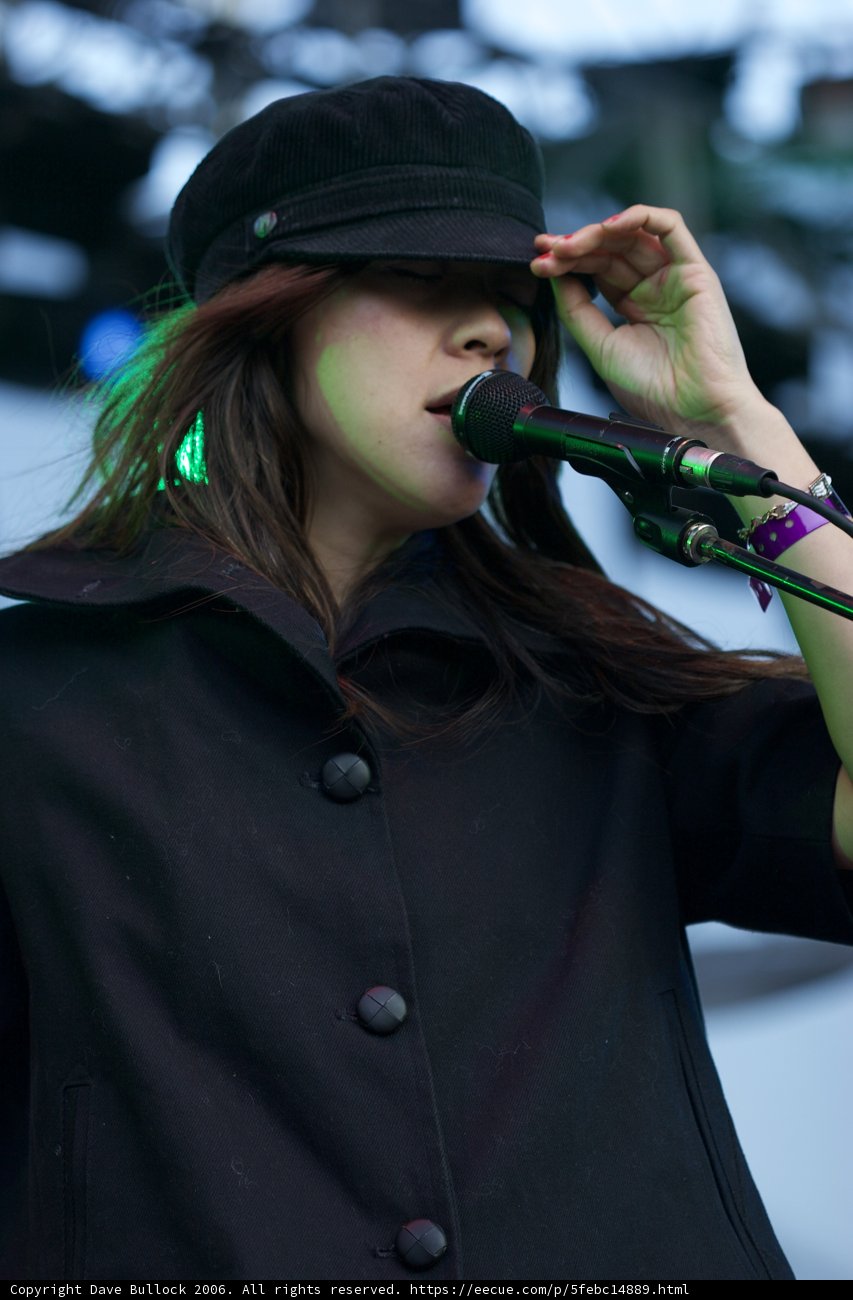 Kazu Makino Takes the Stage with Microphone in Hand and Hat on Head
