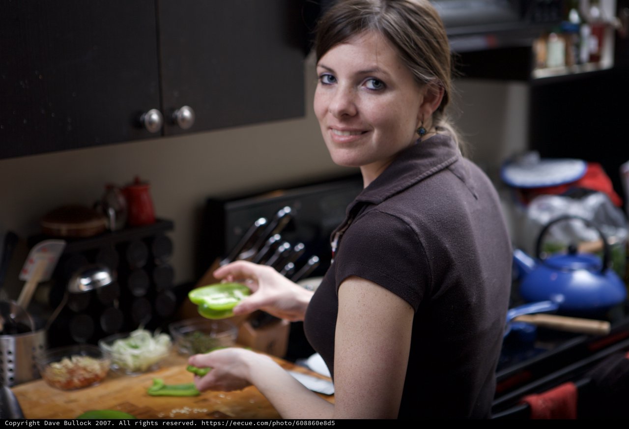 Smiling Woman Chopping Green Peppers in Kitchen