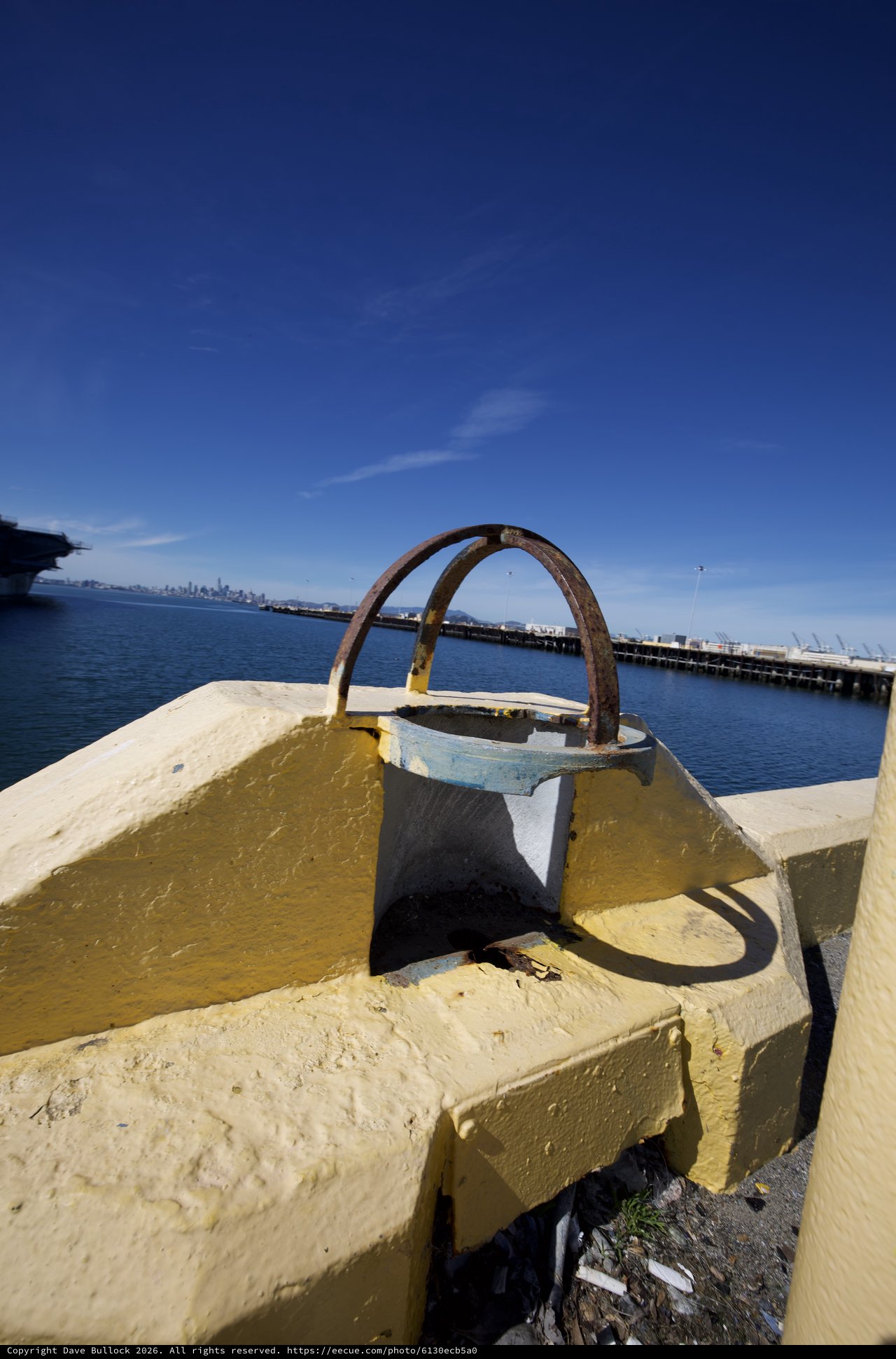 Rusted Mooring Ring on Yellow Painted Bollard at Waterfront