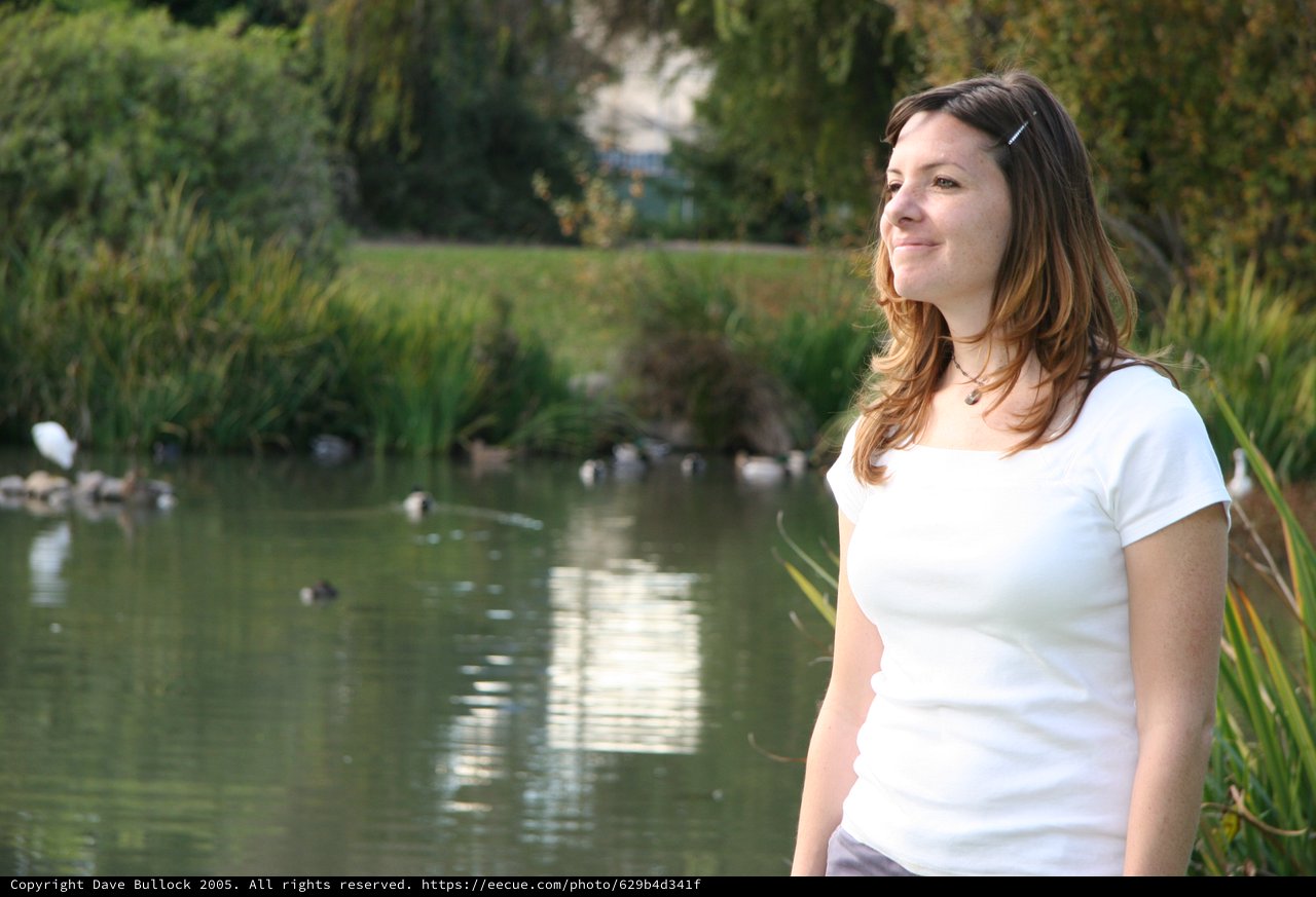 Woman Smiling Beside a Tranquil Park Pond