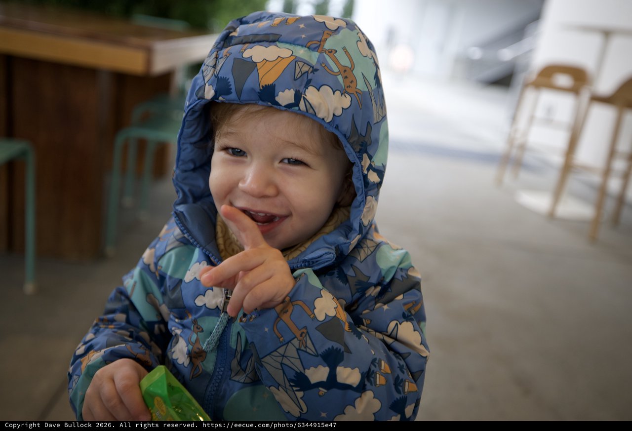 Joyful Toddler in Patterned Rain Jacket at Outdoor Cafe