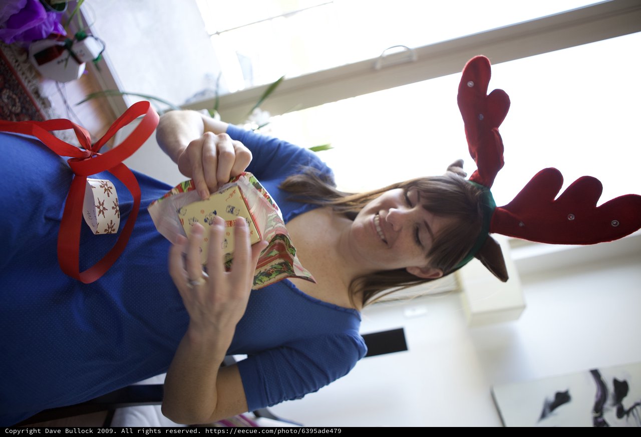 Joyful Woman Unwrapping Christmas Gifts in Reindeer Antlers