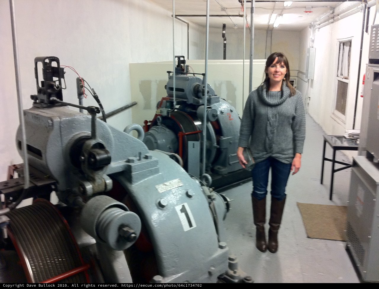 Woman Poses Beside Historic Elevator Machine Room Equipment
