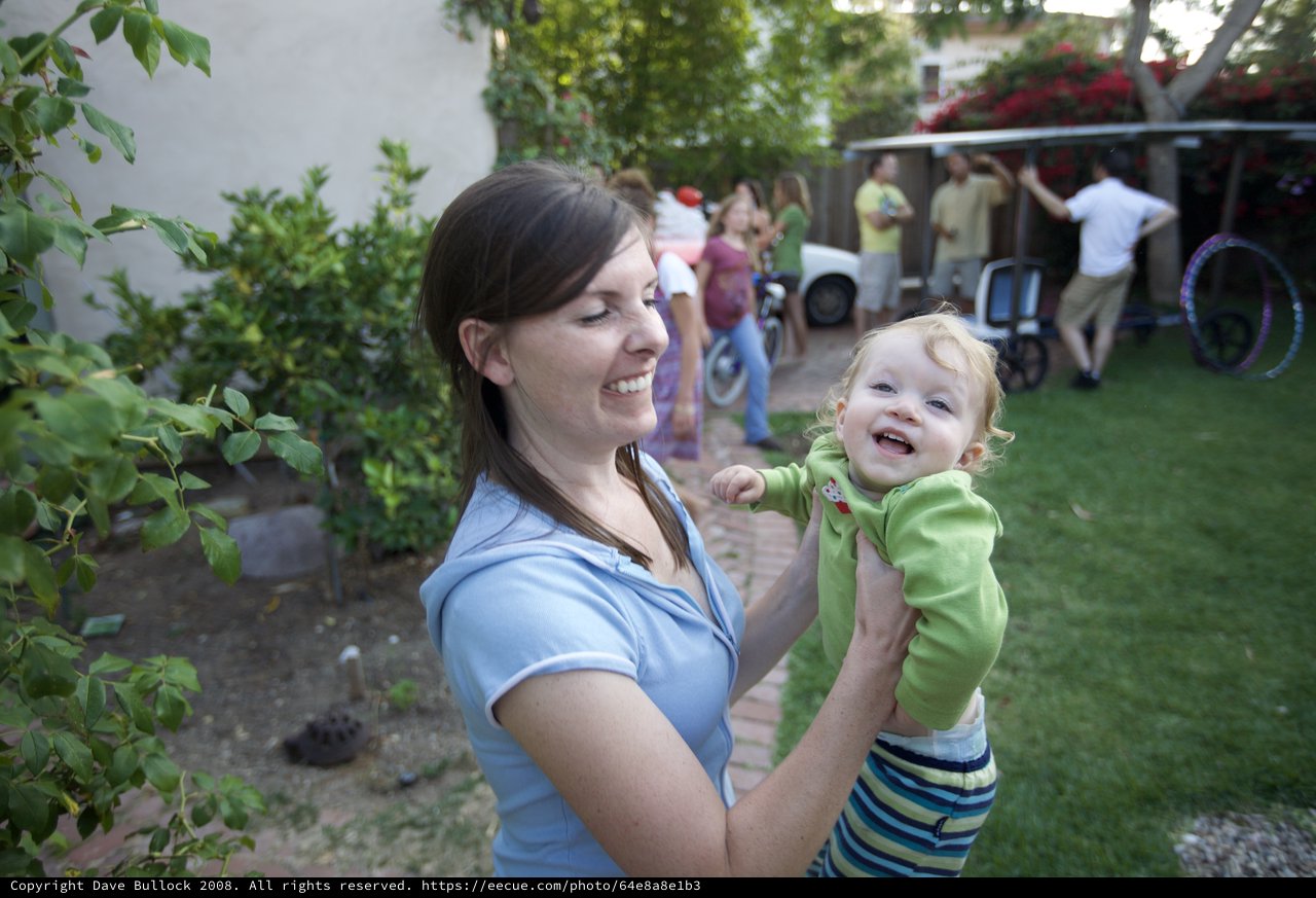 Joyful Mother Lifting Laughing Baby at Backyard Party