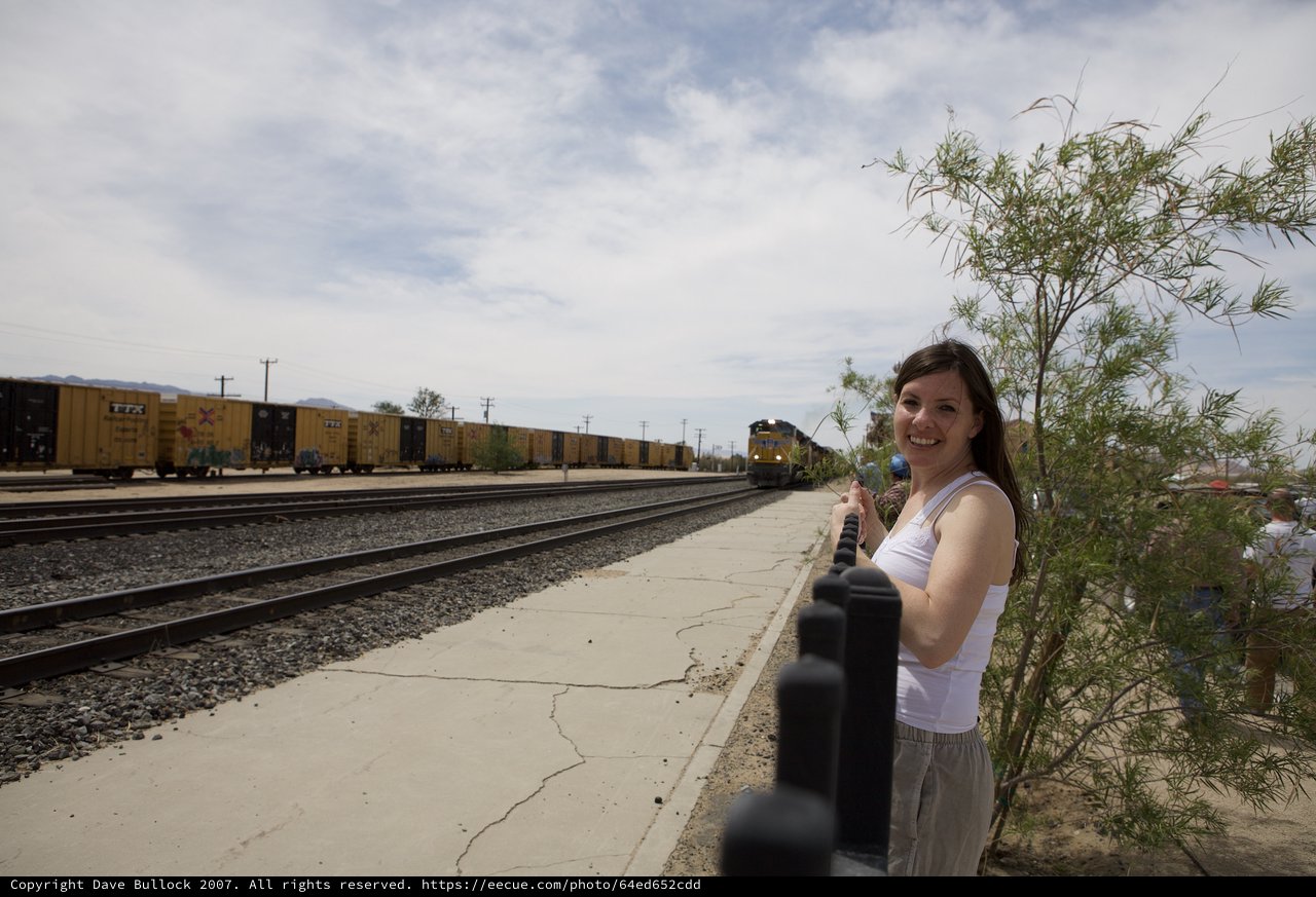 Smiling Woman Watches Freight Train Pass Desert Platform