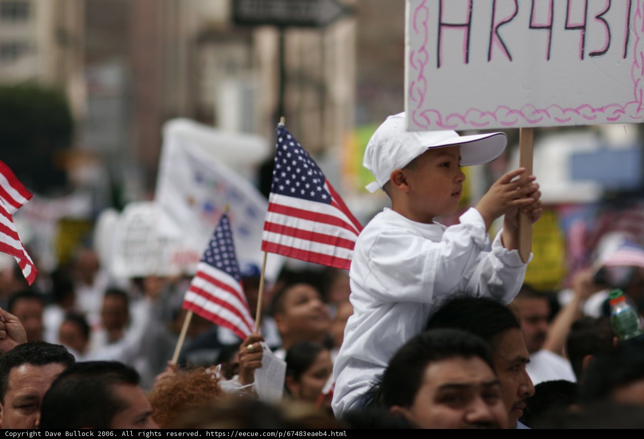 Hat-wearing child holds a sign with cryptic message