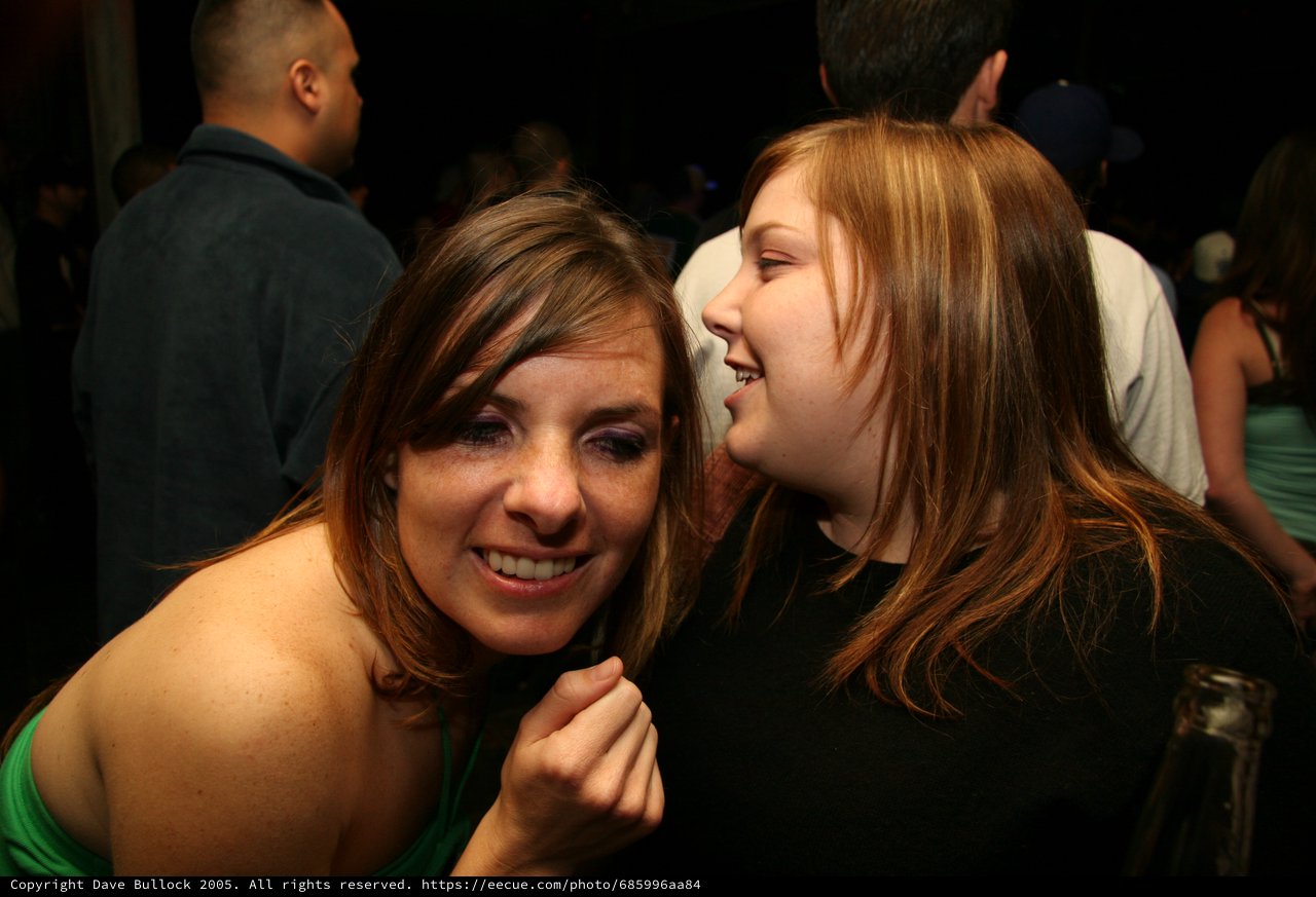 Two Friends Share a Whispered Secret at Nightclub
