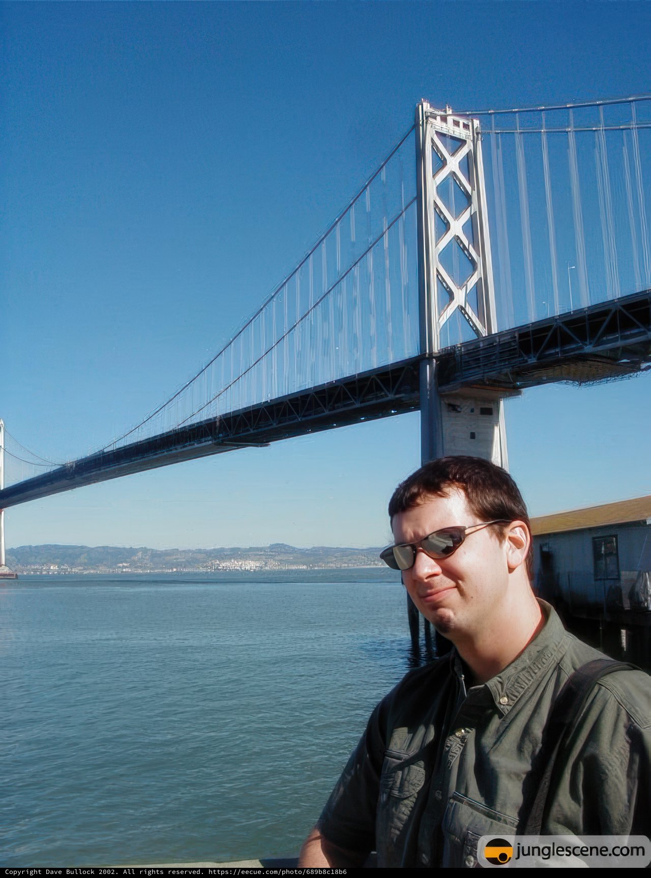 Man in Sunglasses standing in front of Suspension Bridge