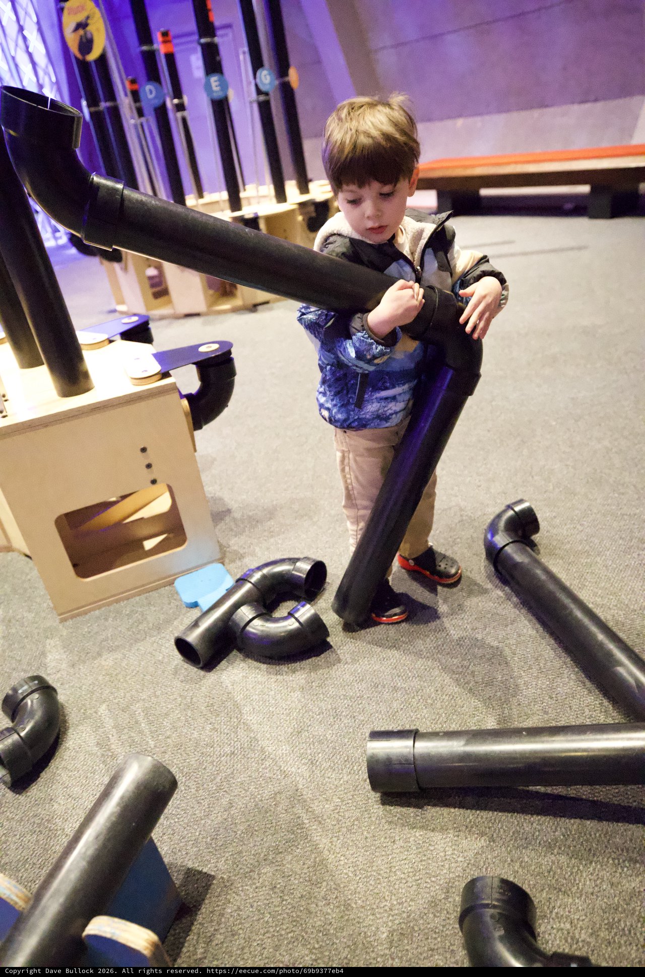 Child Exploring Interactive Pipe Construction Exhibit at Children's Museum