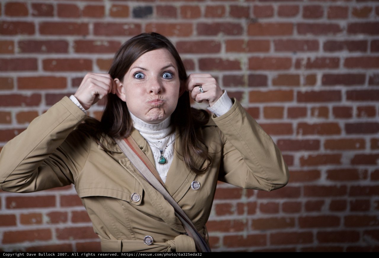 Playful Woman Making Funny Face Against Brick Wall