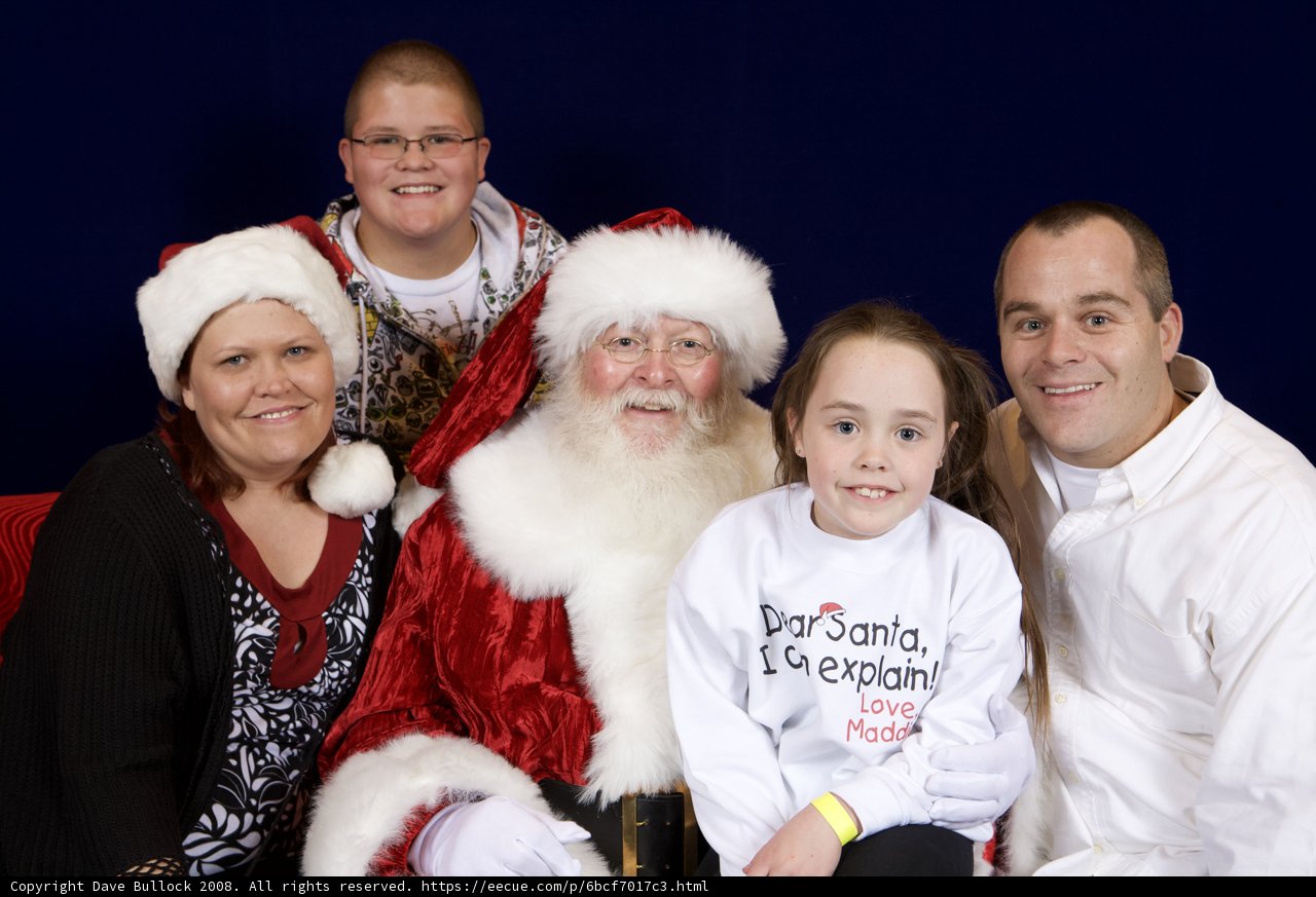 Family of Four Meet Santa Claus Caption: A family of four, including two women and two adults, pose for a festive photo with Santa Claus at the 2008 APC Christmas party. The adults wear glasses and festive clothing, while the children don Santa hats and gloves.