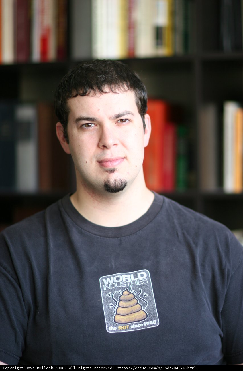 Man in black shirt poses in front of bookshelf