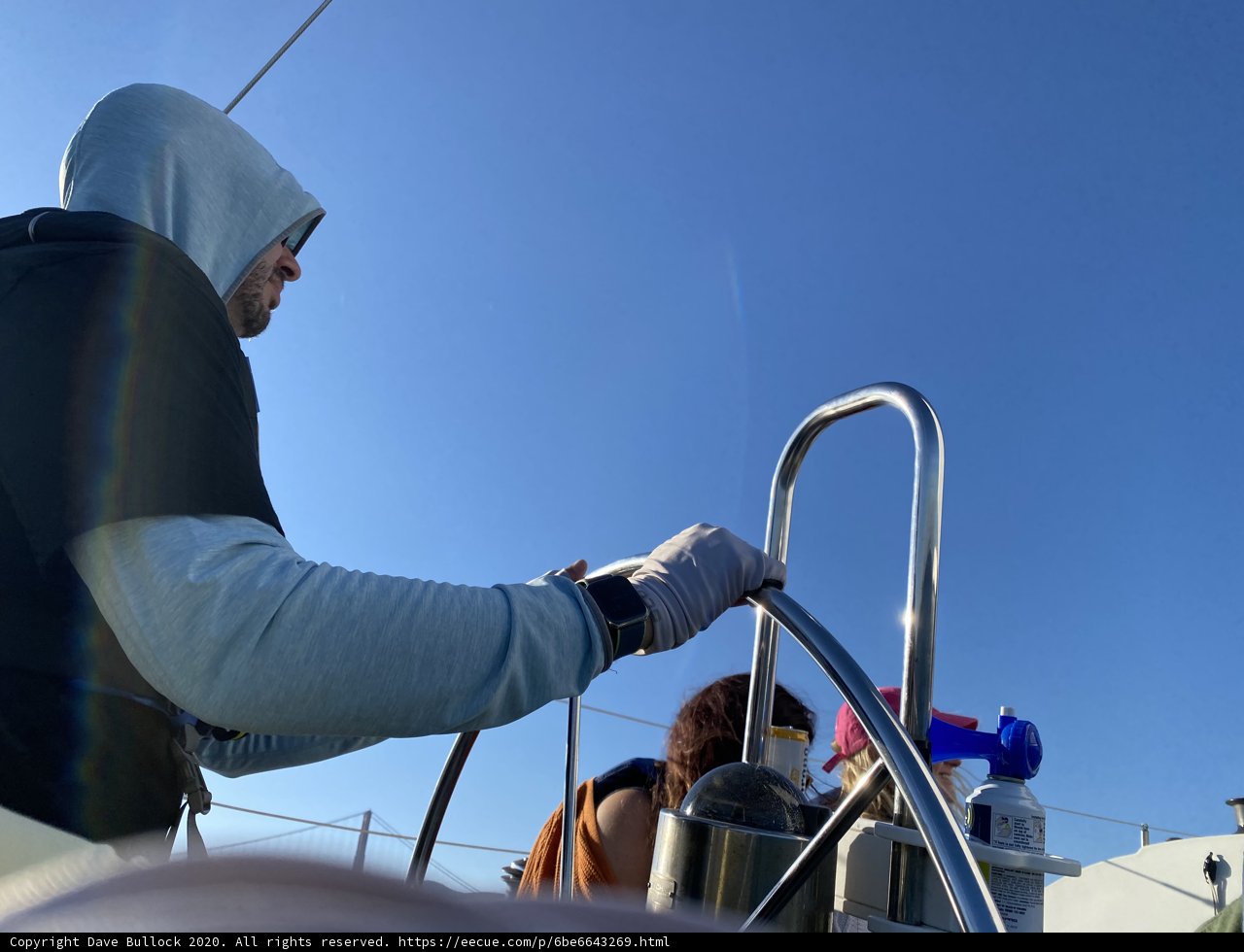 Waterside Worker Caption: A man in a hoodie tends to the hose on a boat while enjoying the blue skies and San Francisco Bay.