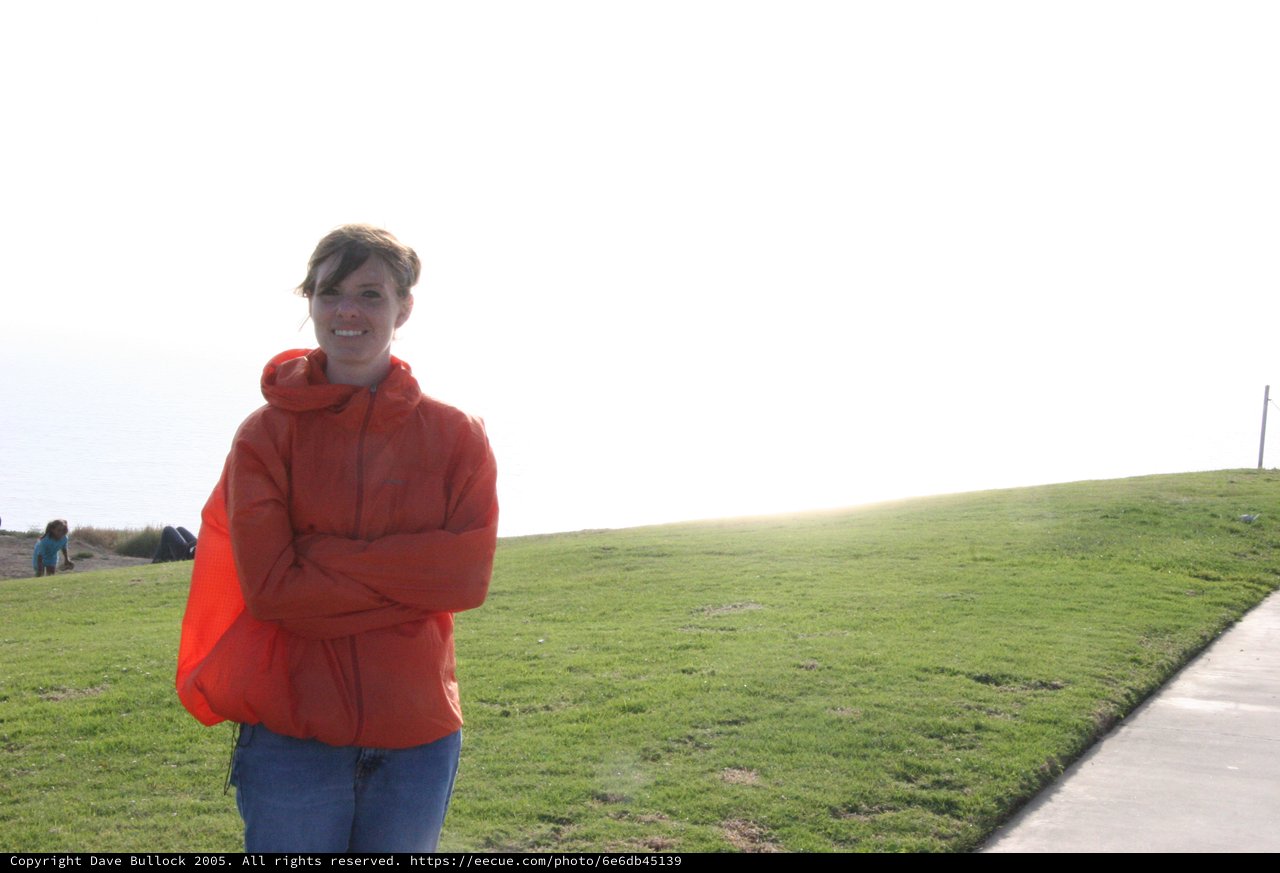 Woman in Red Jacket Smiling at Coastal Park