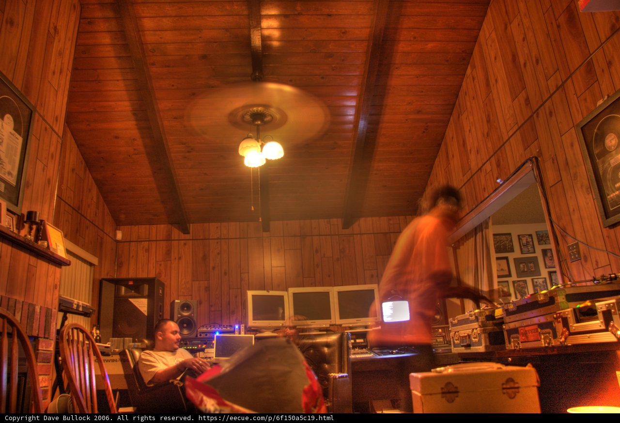 Table Talk Caption: A man enjoying food and music in a cozy plywood room with hardwood flooring, surrounded by paintings and speakers.