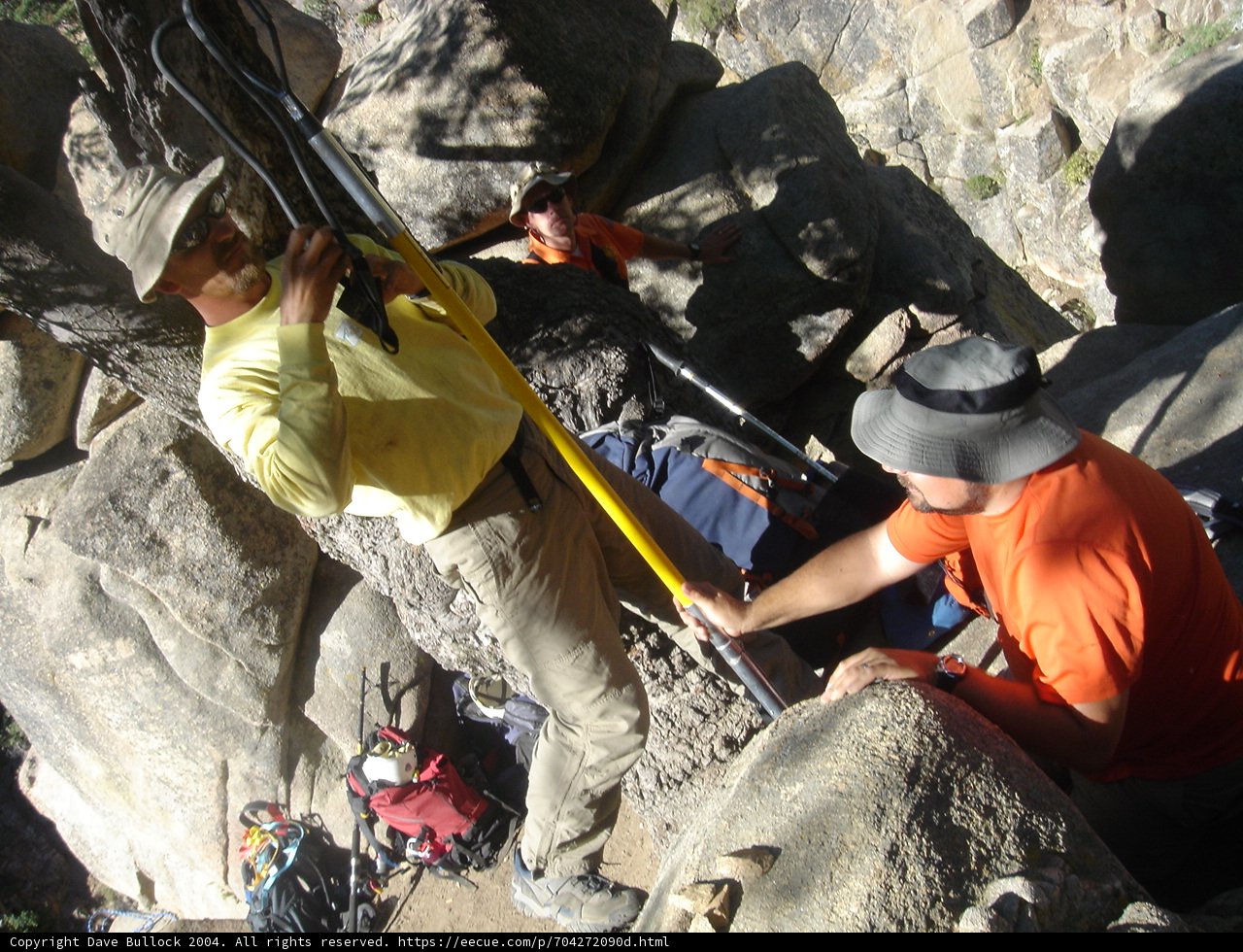 Man Scaling a Slate Rock while Holding a Yellow Pole