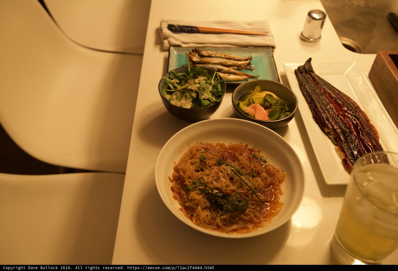Delicious Noodle Dish on Wooden Table Caption: A savory bowl of vermicelli noodles and vegetables with a glass of water placed on a wooden table for a satisfying lunch.