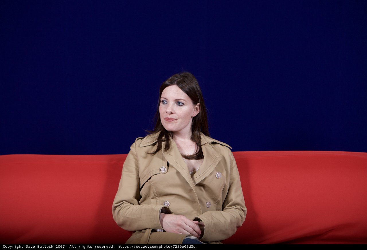 Woman in Trench Coat Seated on Red Sofa