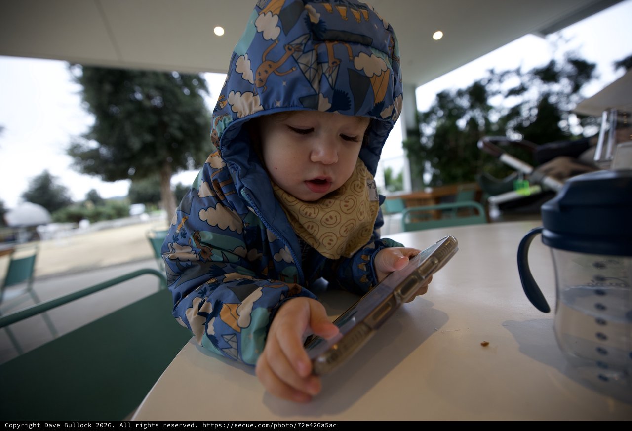 Young Child Using Smartphone at Outdoor Cafe