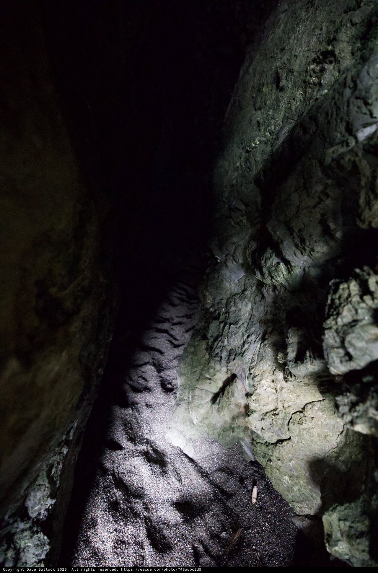 Darkness Ahead: Narrow Cave Passage Illuminated by Flashlight