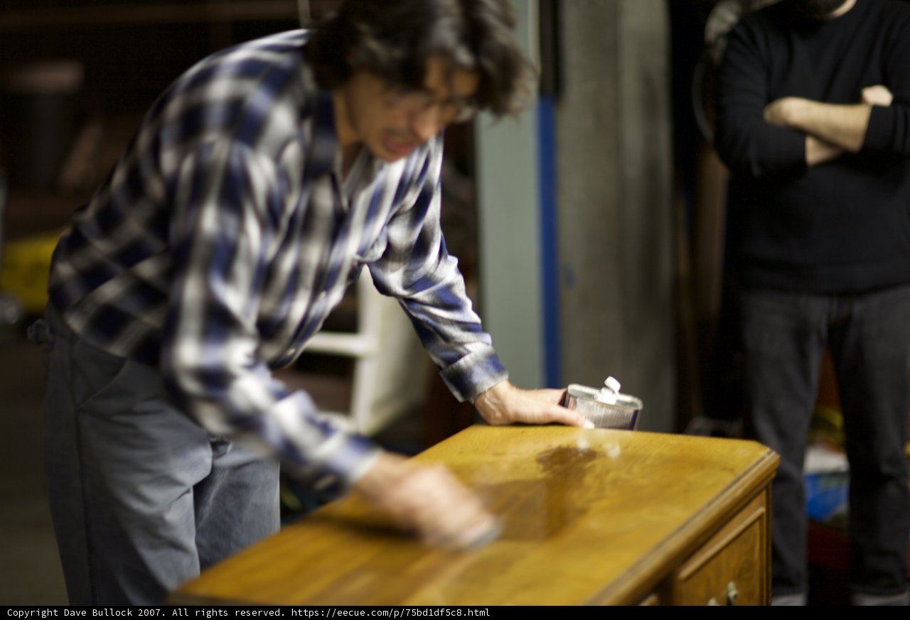 Polishing the Plywood Table Caption: A man's hand carefully polishes a plywood table while his colleague watches on.