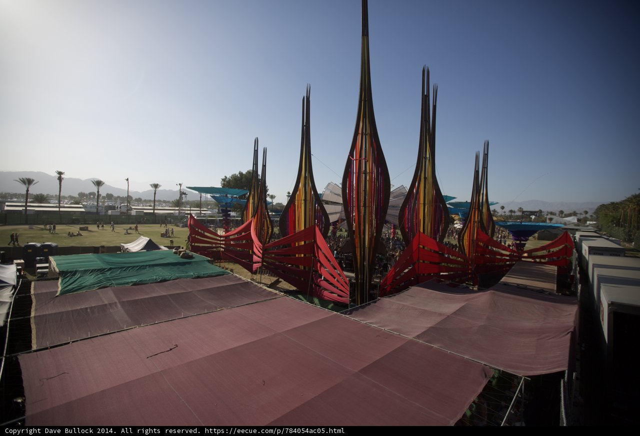 Colorful Flags Flying High in Coachella | Caption: A large tent adorned with colorful flags providing shelter and a vibrant scenery at Coachella 2014 in Indio, United States. The blue sky and waterfront complement the architecture of the tent creating the perfect outdoor experience.