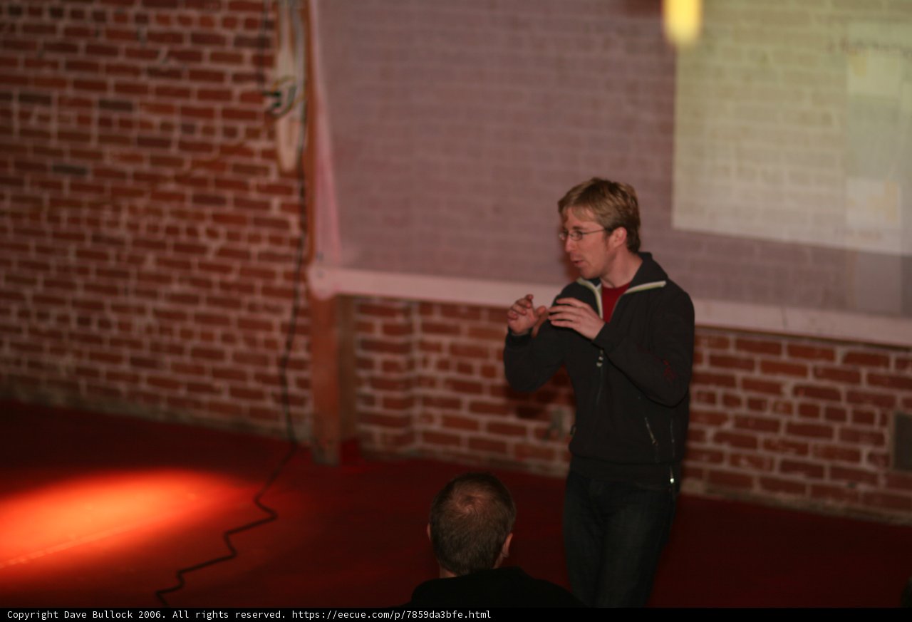 Man Speaking with Microphone in Hand in front of Brick Wall