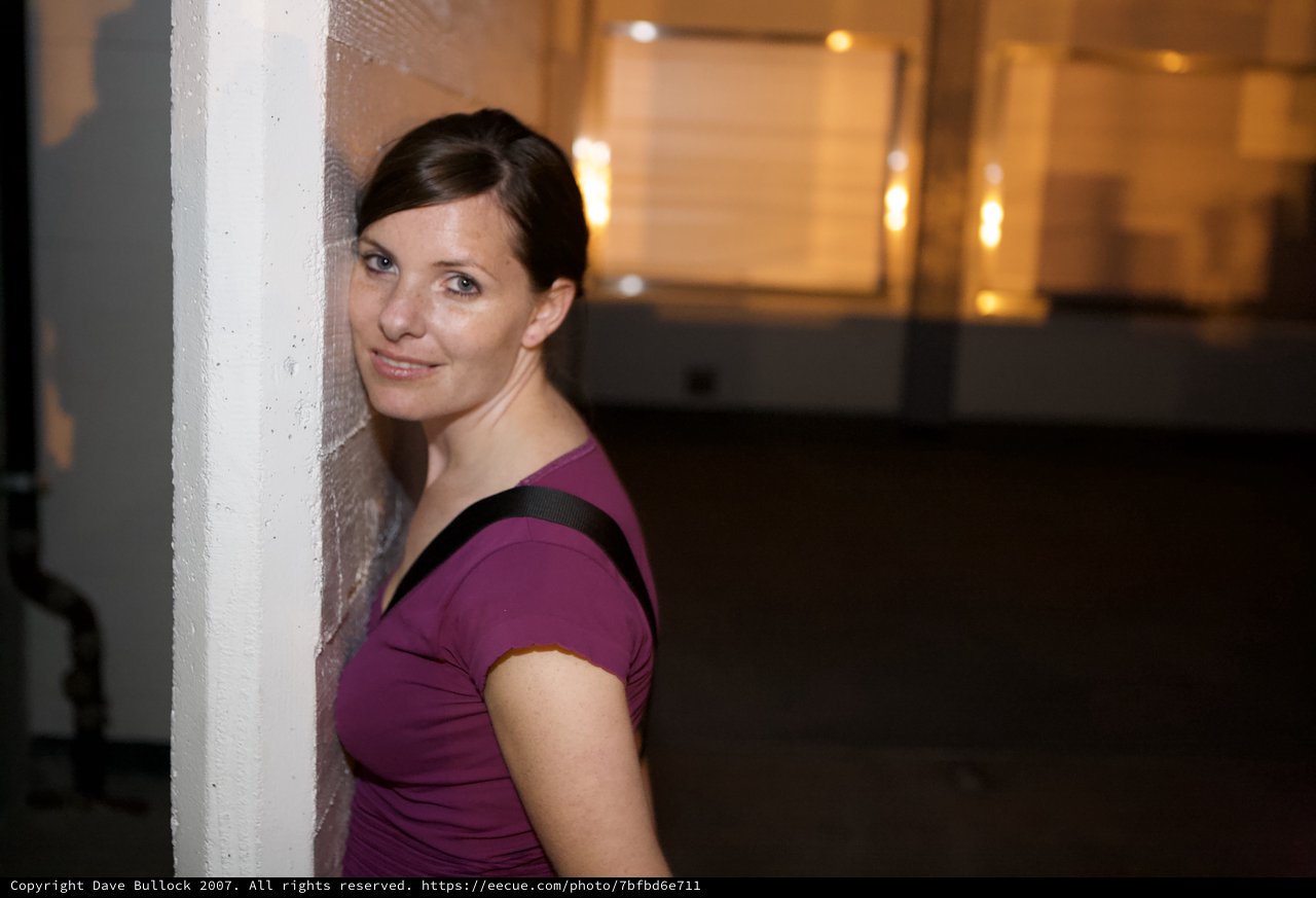 Woman Leans Against Wall With Playful Smile