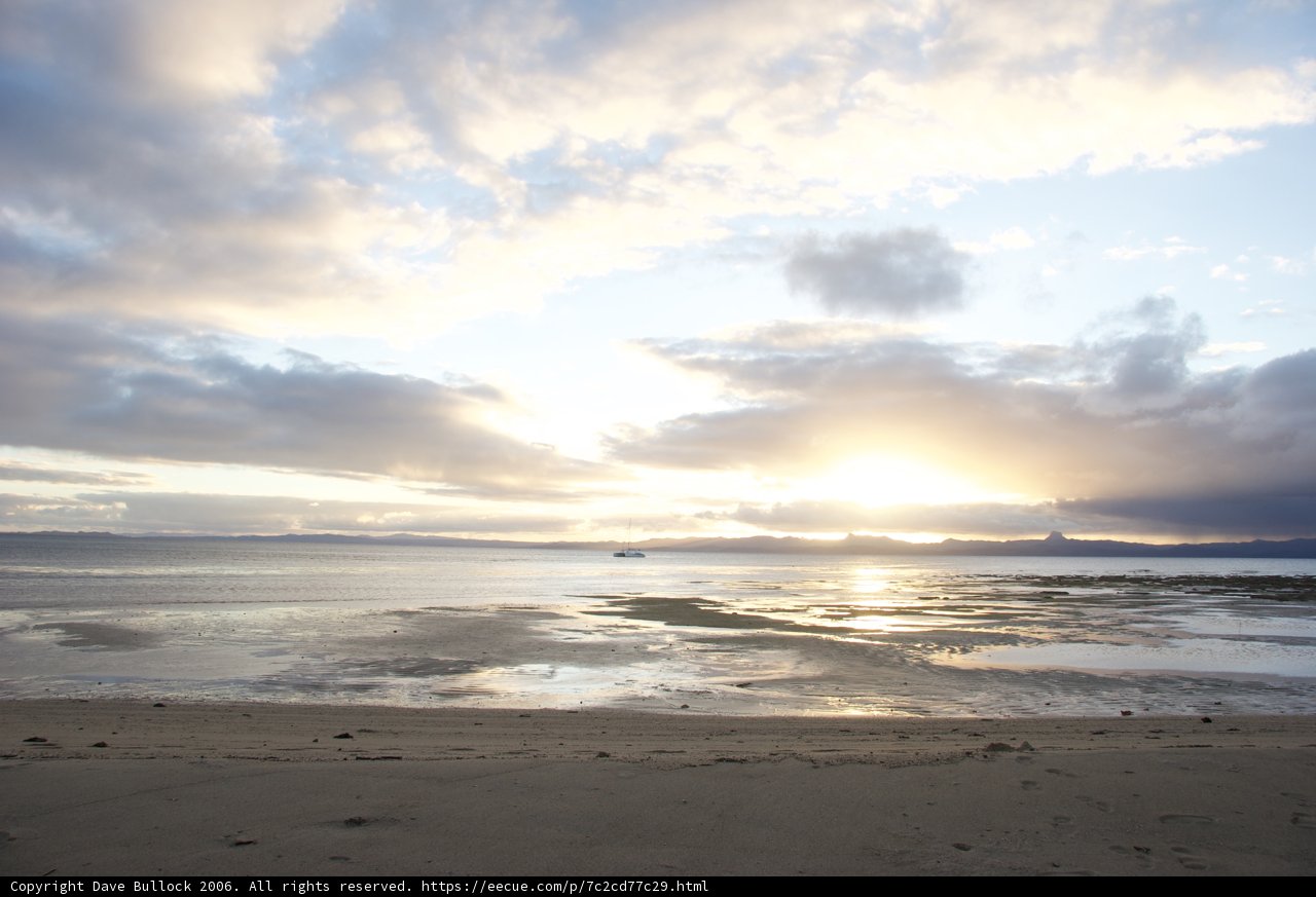 Serene Beach with a Boat and Clouds at Sunset
