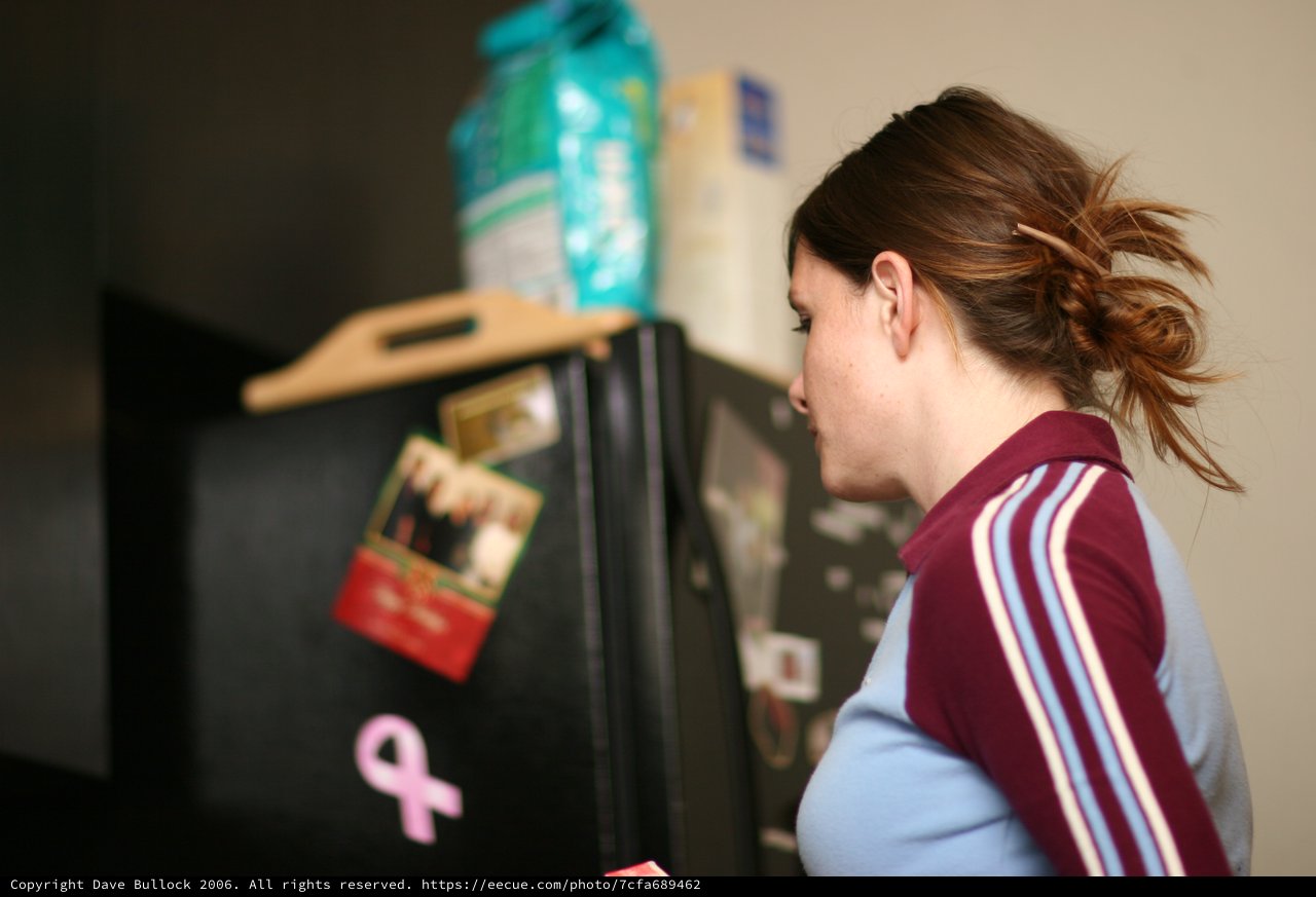Young Woman Peering Into Black Refrigerator at Night